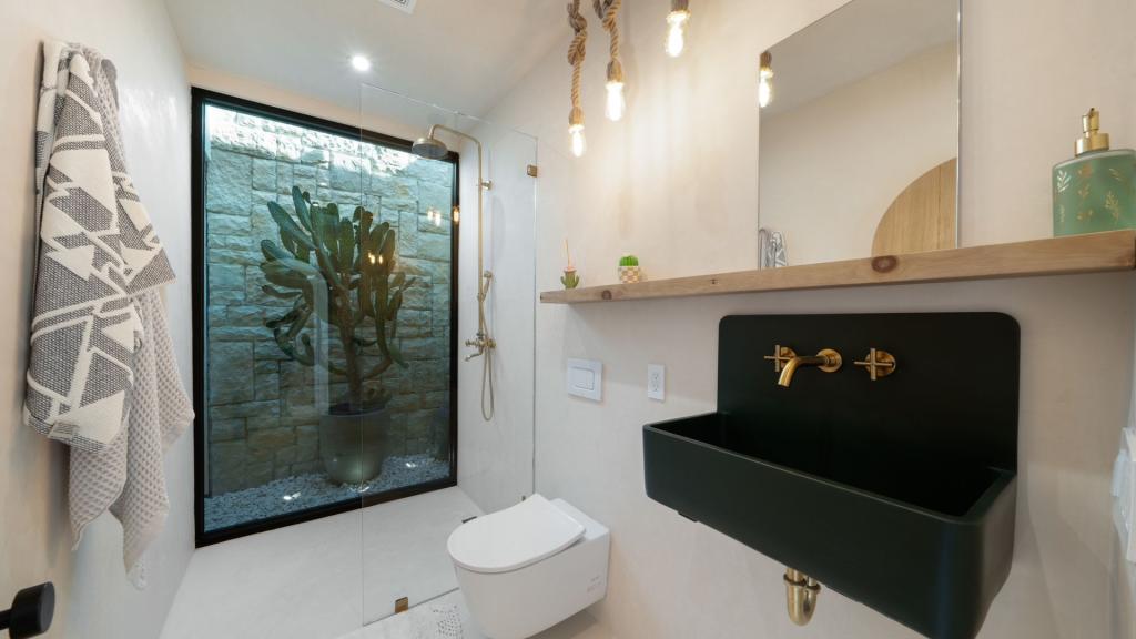 Modern bathroom remodel in San Diego with a black wall-mounted sink, brass fixtures, glass shower, and natural stone accent wall
