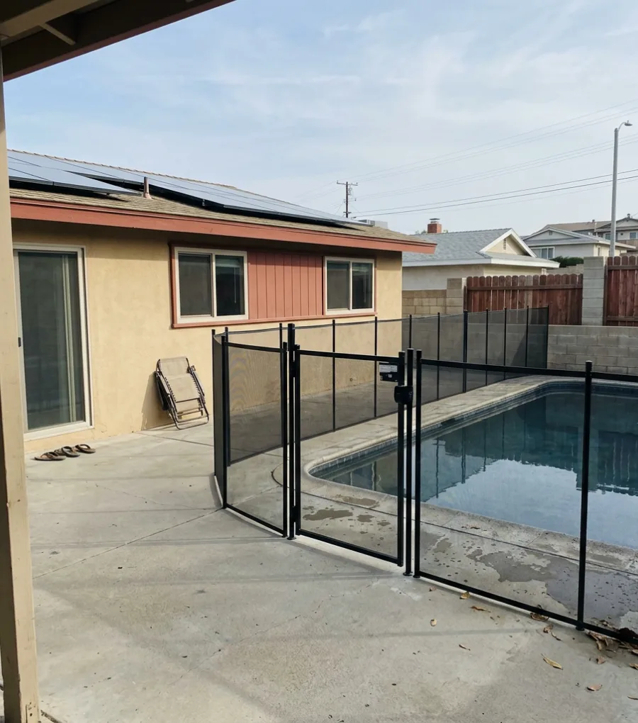 Black aluminum pool safety fence with self-closing gate around a backyard pool